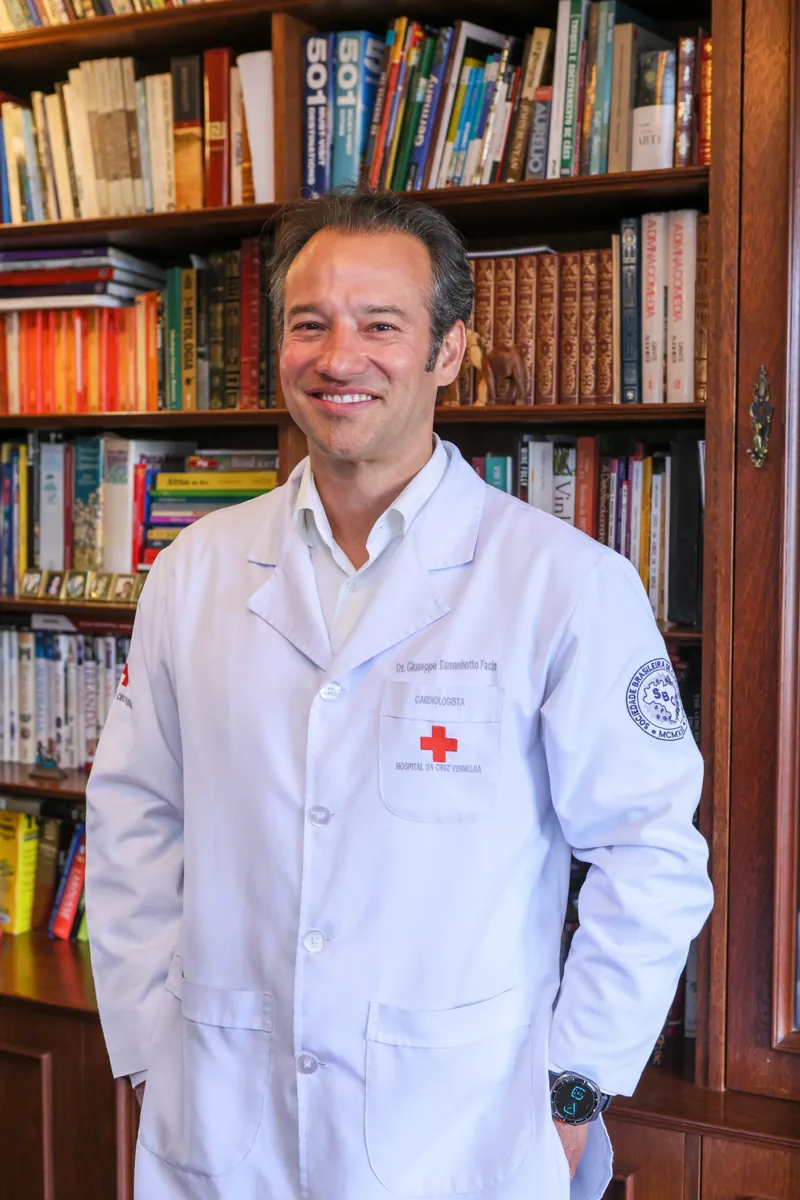 Dr. Giuseppe Esmanhotto Facin, cardiologista, de jaleco em frente a uma estante de livros